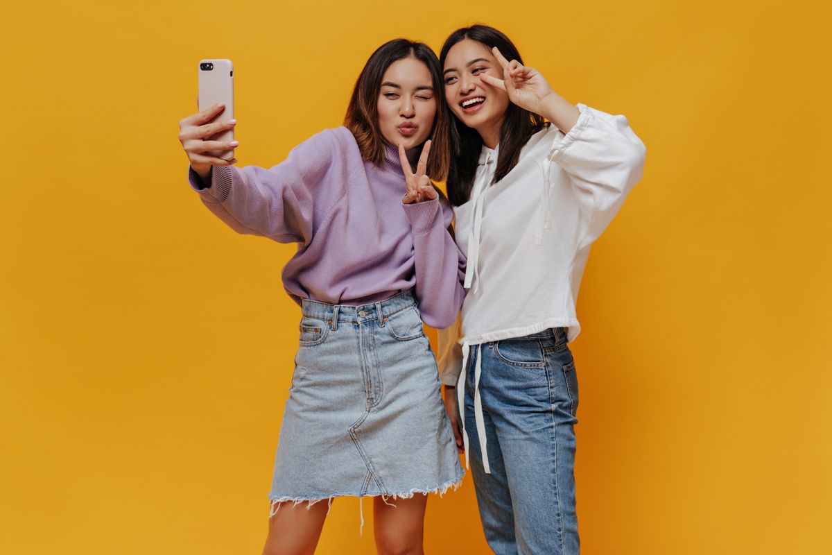 Young brunette asian women take selfie on orange wall
