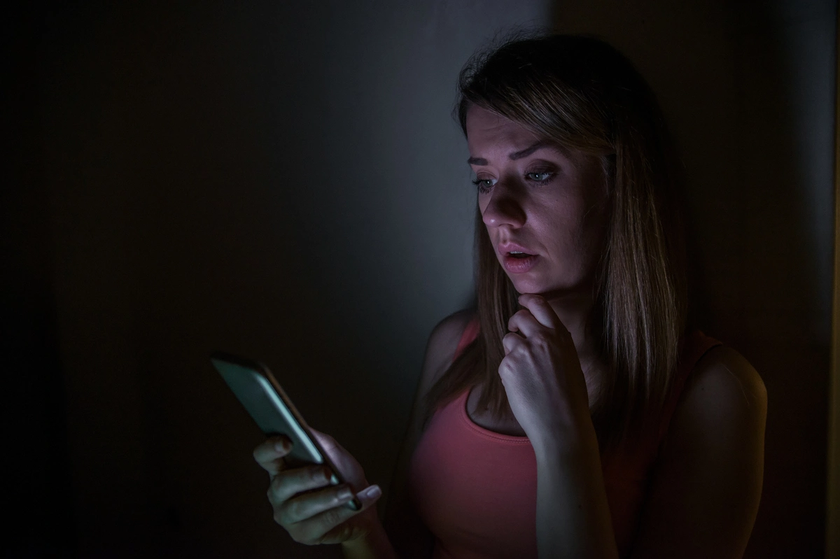 sad news fear mongering young woman with mobile phone reads message at night at home